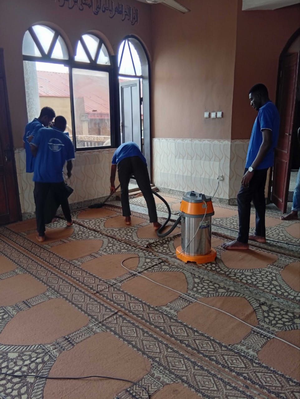 Team vacuuming patterned center rug inside a mosque