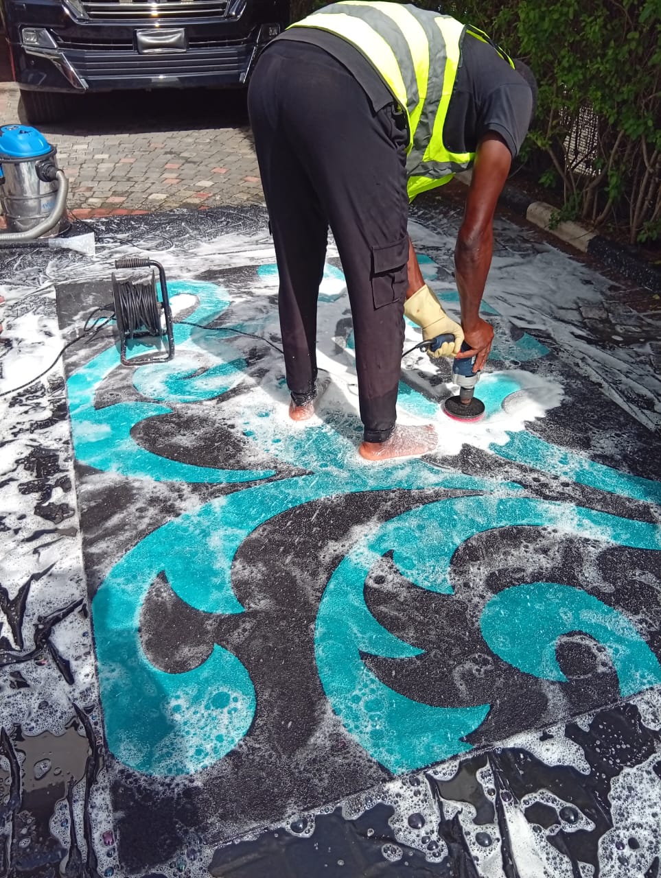 Operator polishing turquoise patterned area rug with a rotary scrubber