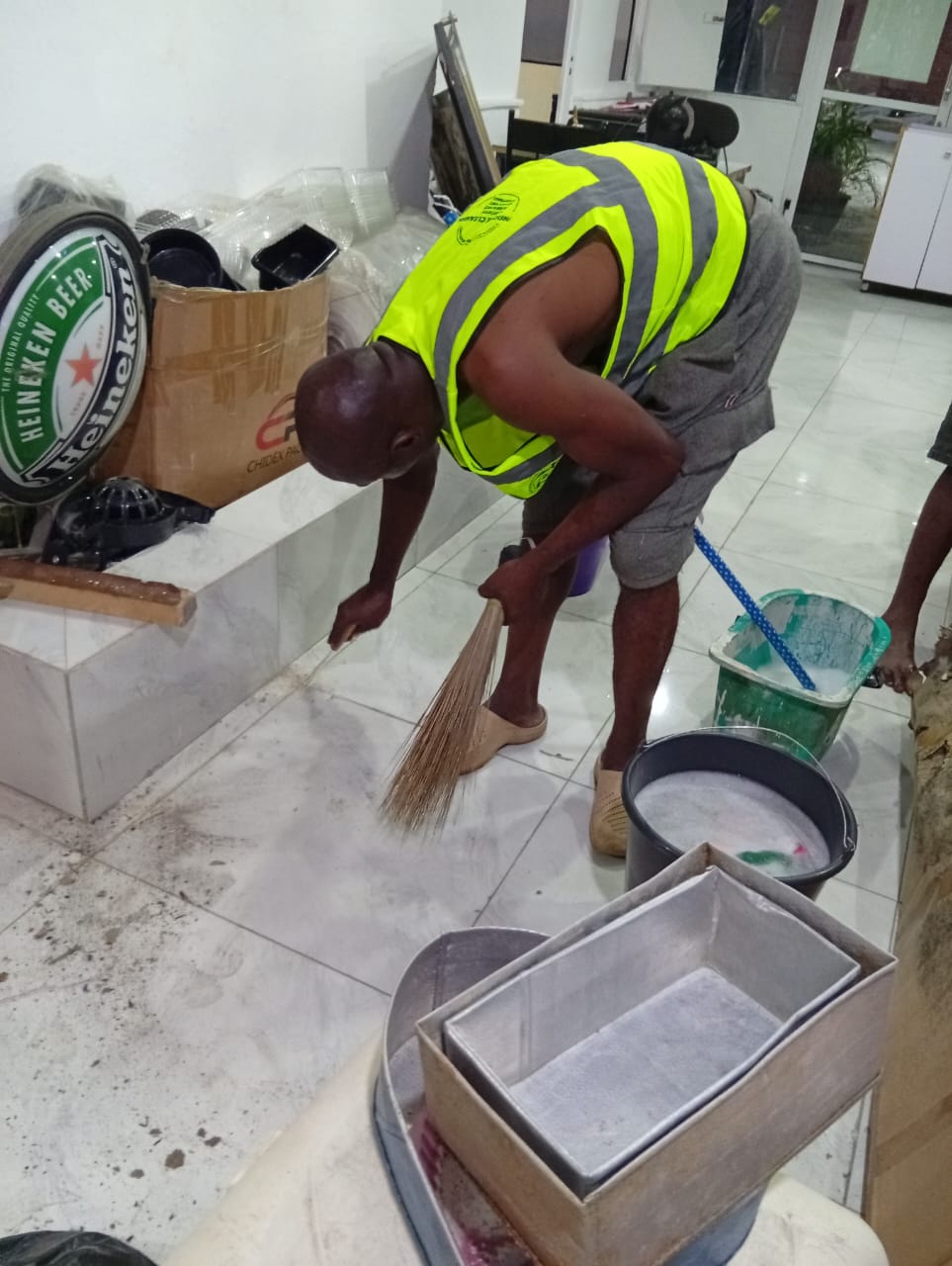 Worker in safety vest sweeping tiled floor during commercial cleanup