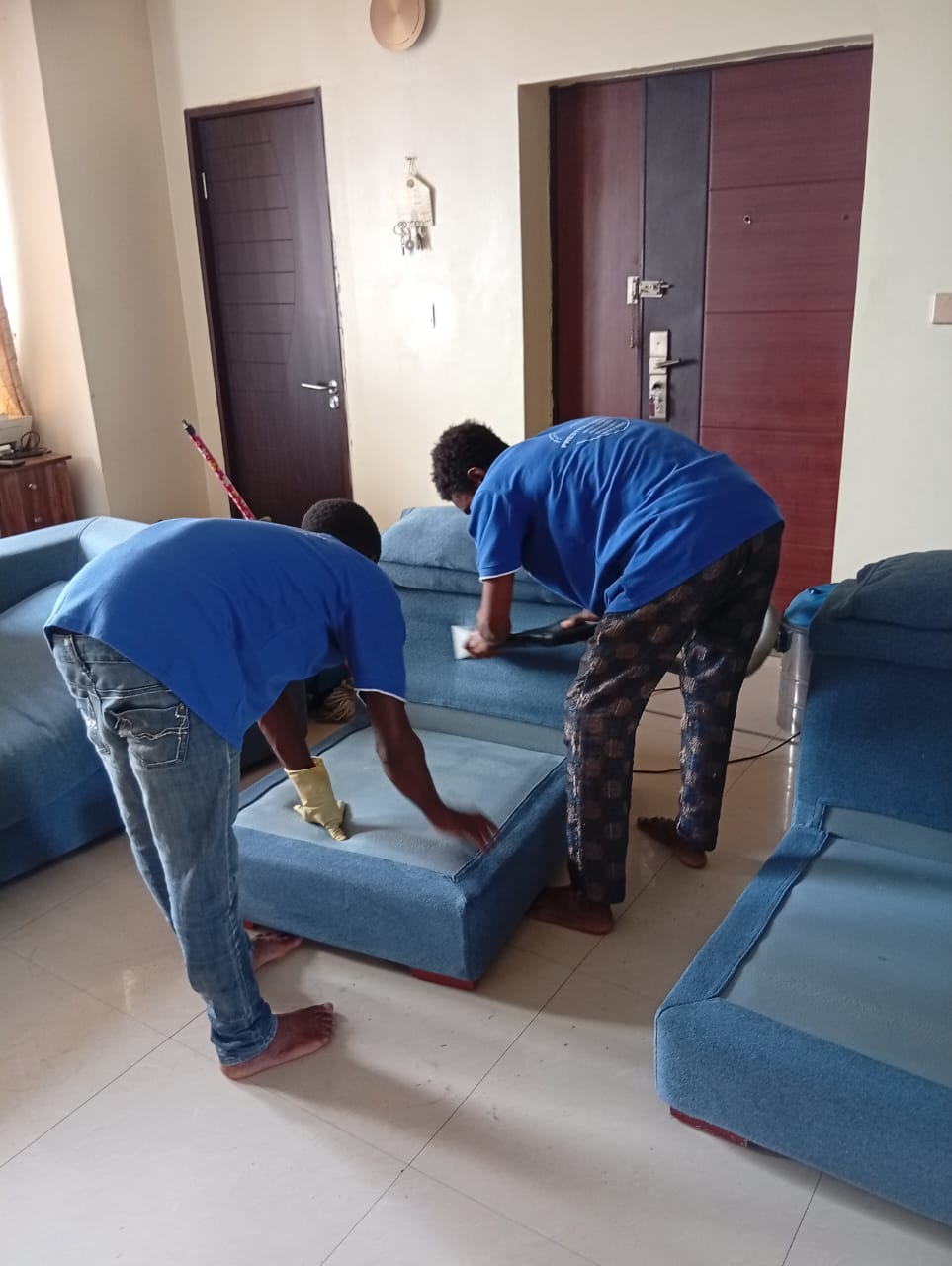 Two Prestige Cleaners staff scrubbing blue sofa cushions in a residence