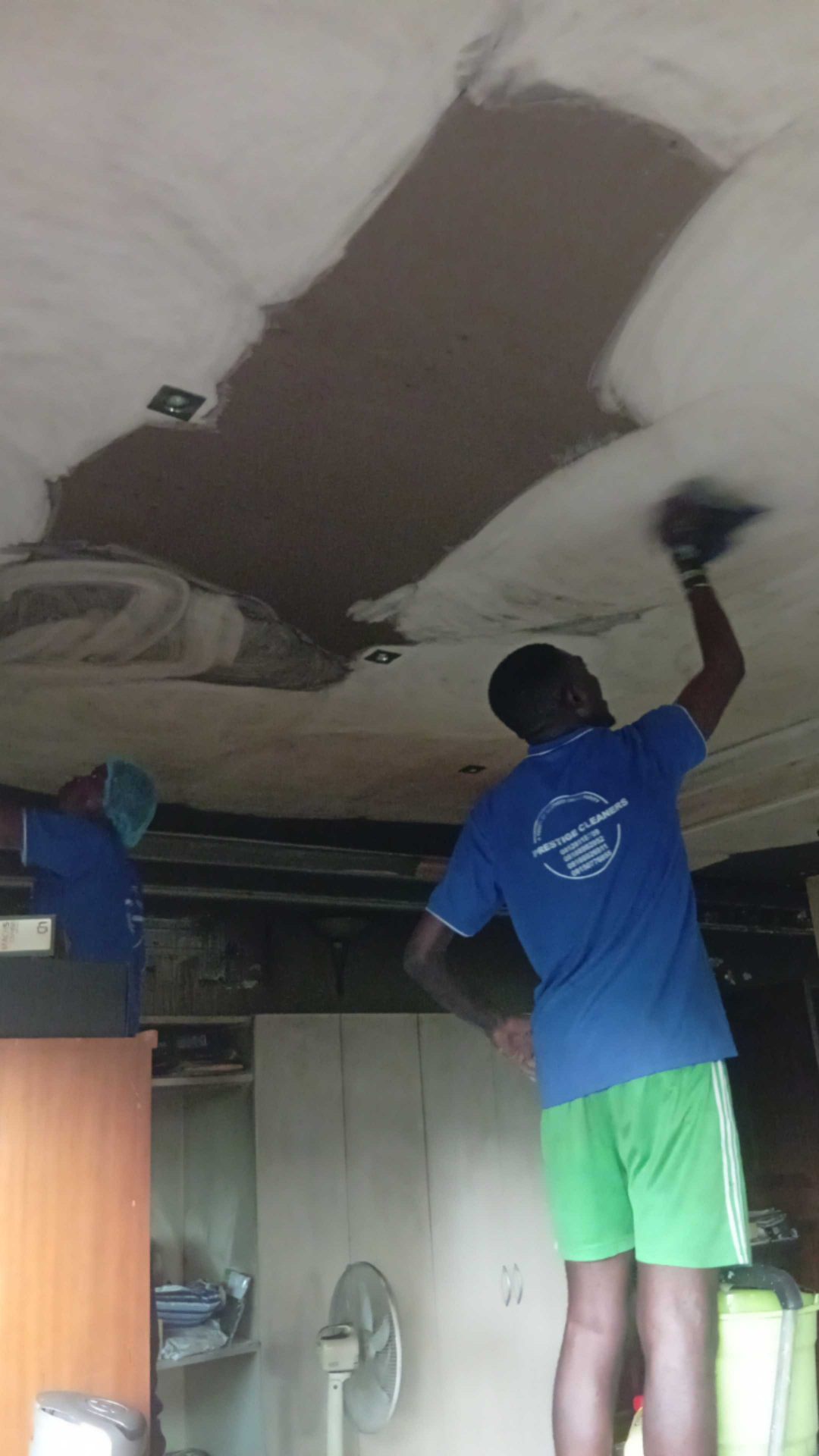 Staff in blue Prestige Cleaners uniform brushing residential ceiling