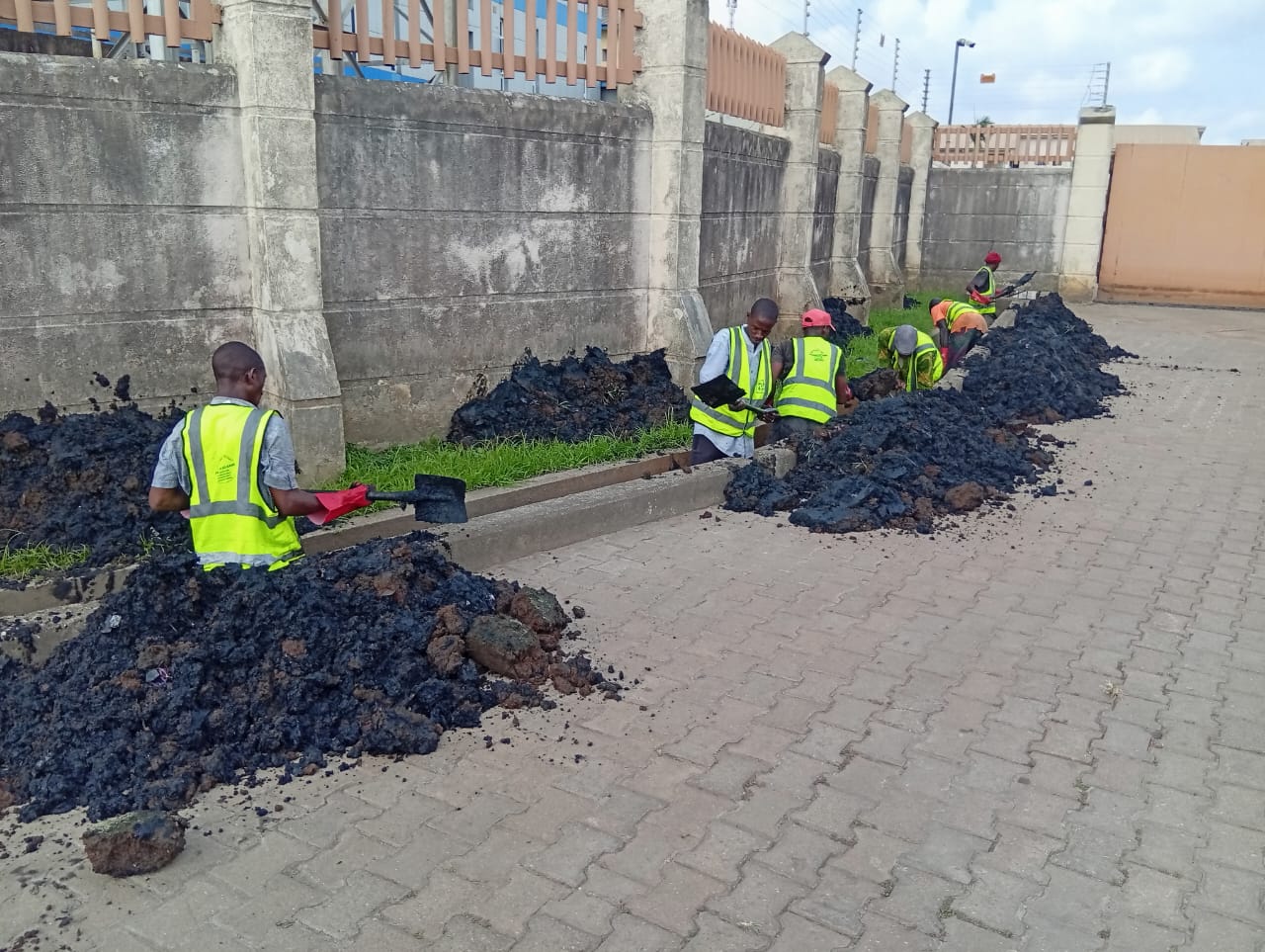 Team in reflective vests clearing thick mud from a compound gutter